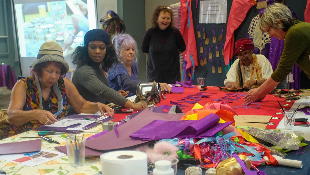 A group of women making colourful banners by hand for the Age Well Festival