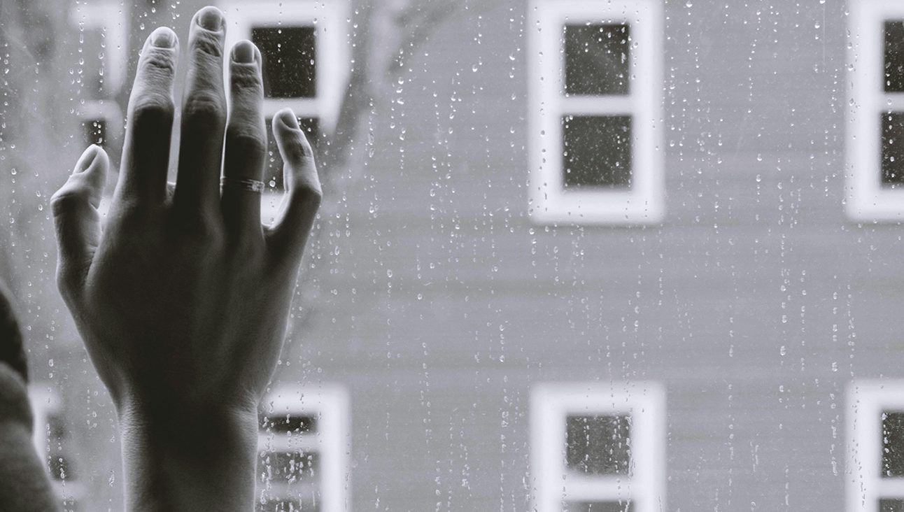 A black and white photo of a hand on a window pane
