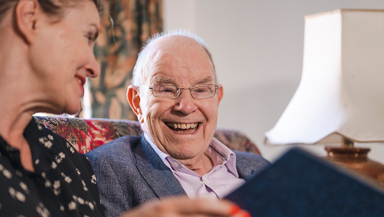 An older man smiling while being shown something by a woman