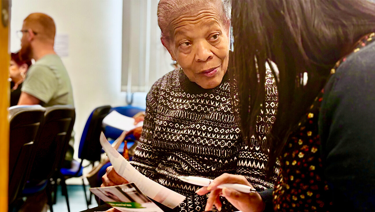 An older black woman holding a pamphlet speaks with another woman