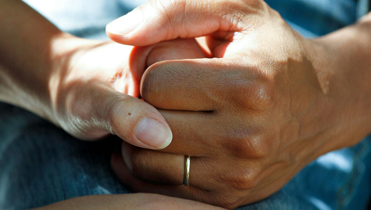 A white hand and a black hand interlinked. There is a gold ring on the black hand