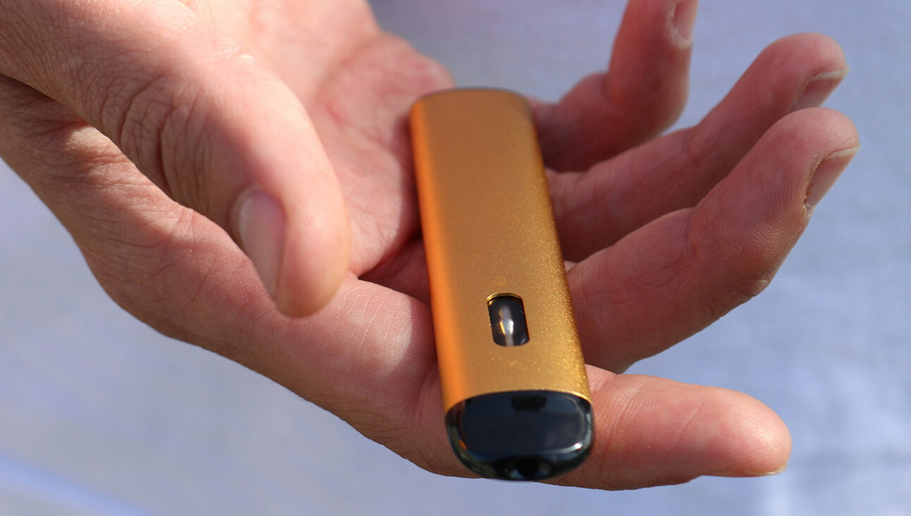 A white person's hand holding out a gold vape
