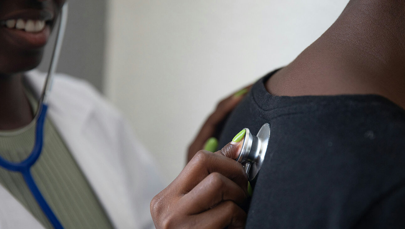 A black female GP using a stethoscope on the back of a patient