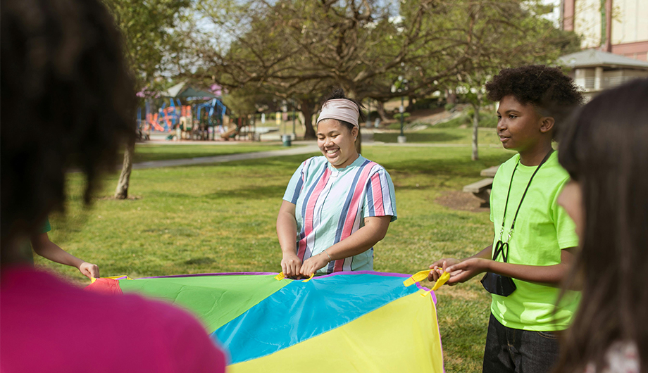 A group of young people in a park playing with a multi-coloured piece of fabric
